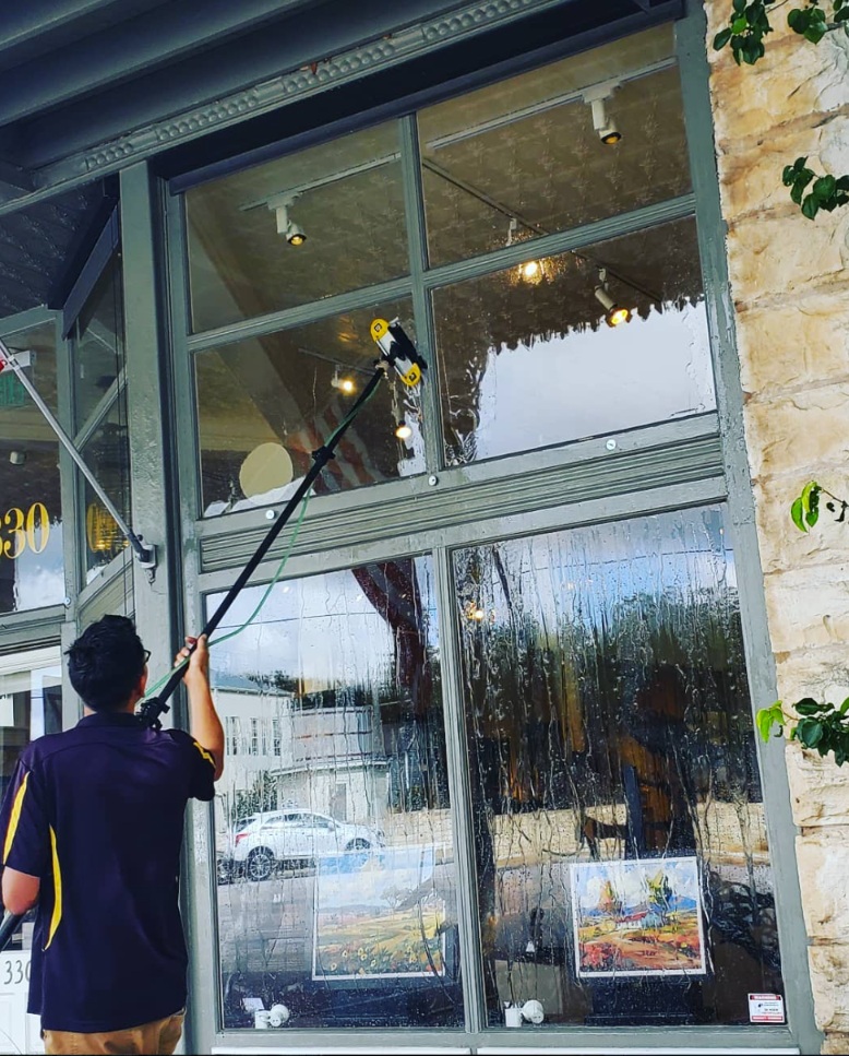 Water-fed pole cleaning tall storefront glass on a Main Street shop